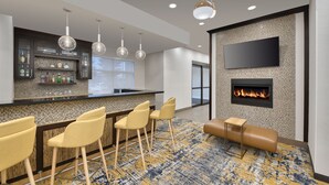 Un espace bar moderne avec un mur recouvert de carreaux, des tabourets de bar, un téléviseur à écran plat et une cheminée.