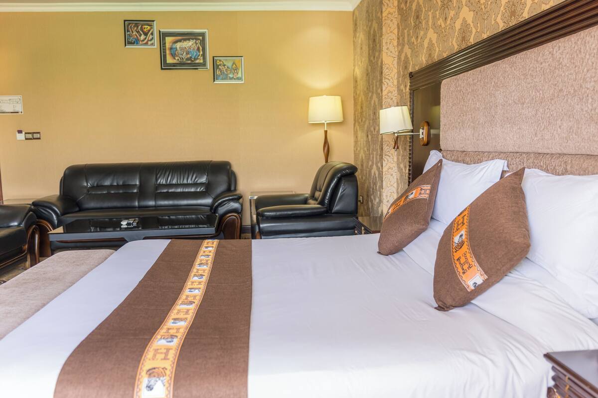 A hotel room with a large bed, two black leather sofas, a wall-mounted lamp, and framed artwork.