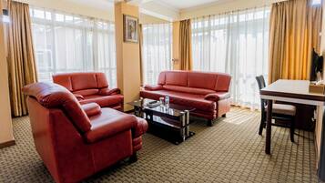 A hotel room with a red leather sofa, a glass coffee table, and a dining table.