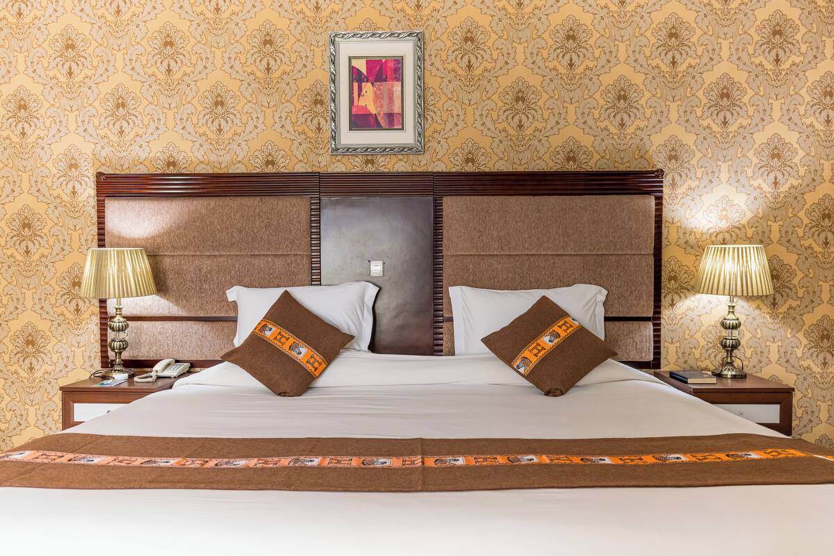 A large bed with a wooden headboard, two bedside tables with lamps, and a framed picture above the bed.