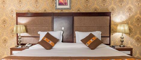 A large bed with a wooden headboard, two bedside tables with lamps, and a framed picture above the bed.