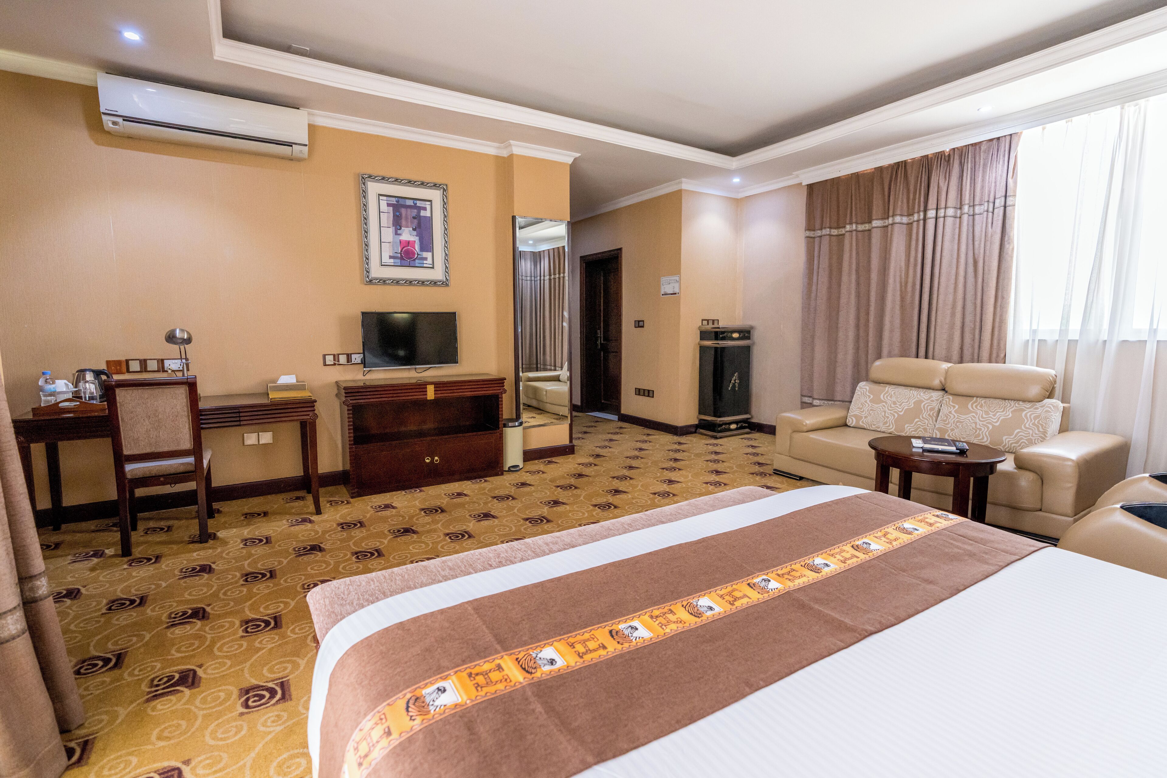 Ein Hotelzimmer mit einem großen Bett, einem Schreibtisch mit Stuhl, einem Fernseher, einer Couch und einem kleinen Tisch.