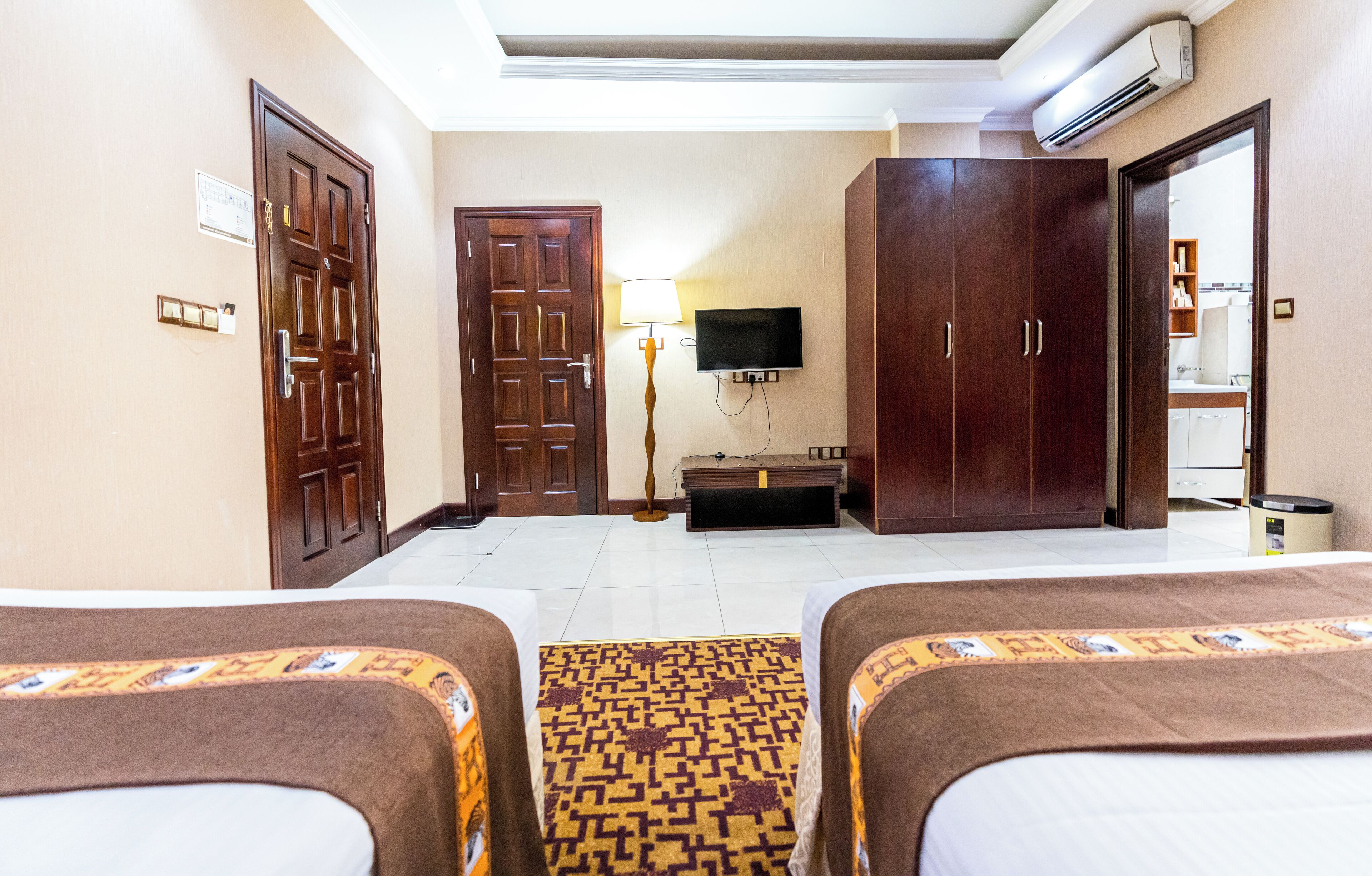 A hotel room with two beds, a television, a wardrobe, and a desk with a lamp.