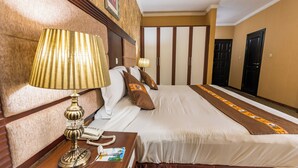 A hotel room with a large bed, a bedside table with a lamp, a telephone, and a magazine.