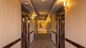 A hotel corridor with mirrored walls, a patterned carpet, and a central light fixture.