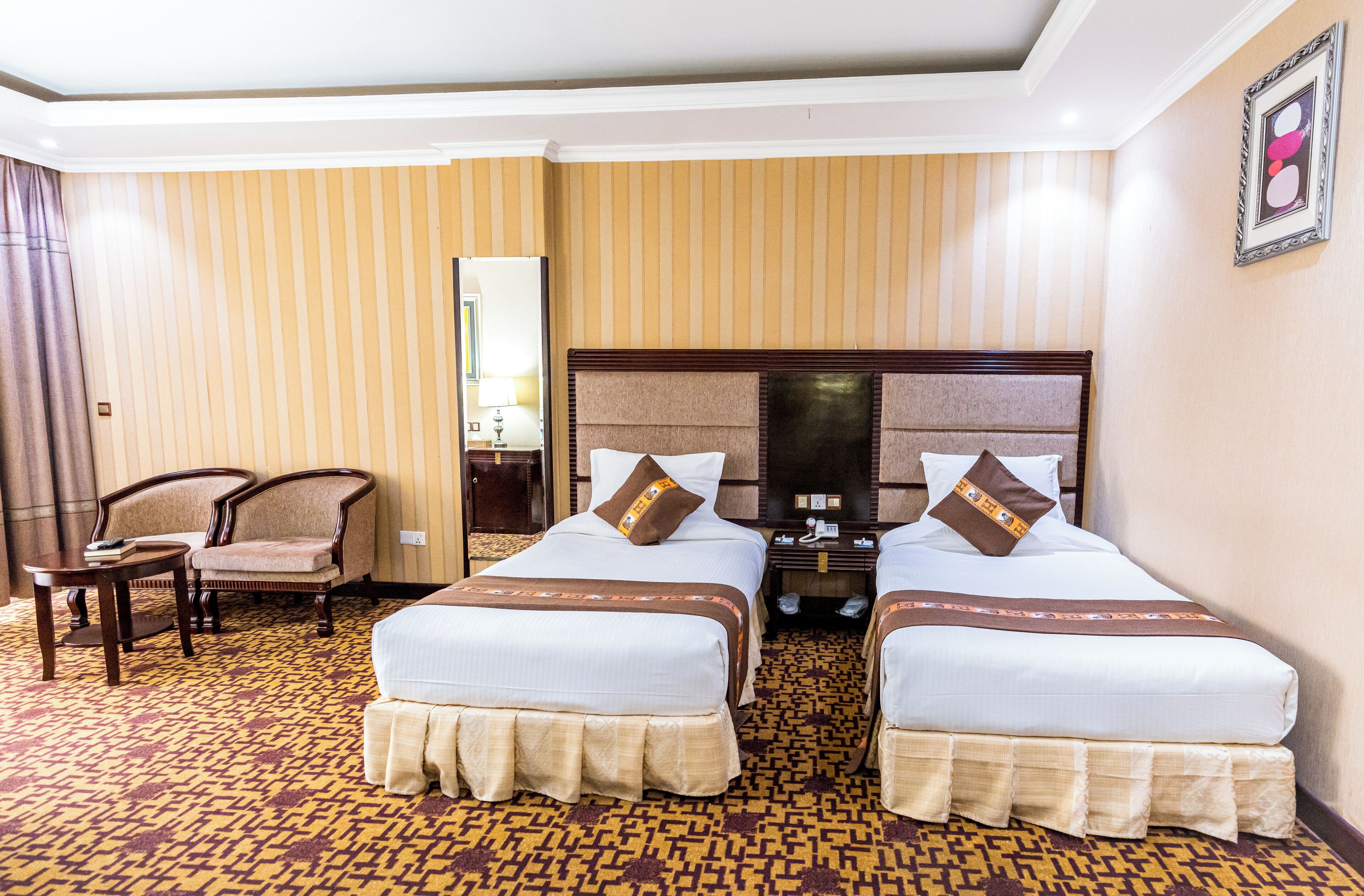 Habitación de hotel con dos camas, una silla, una mesita de noche y una alfombra estampada.
