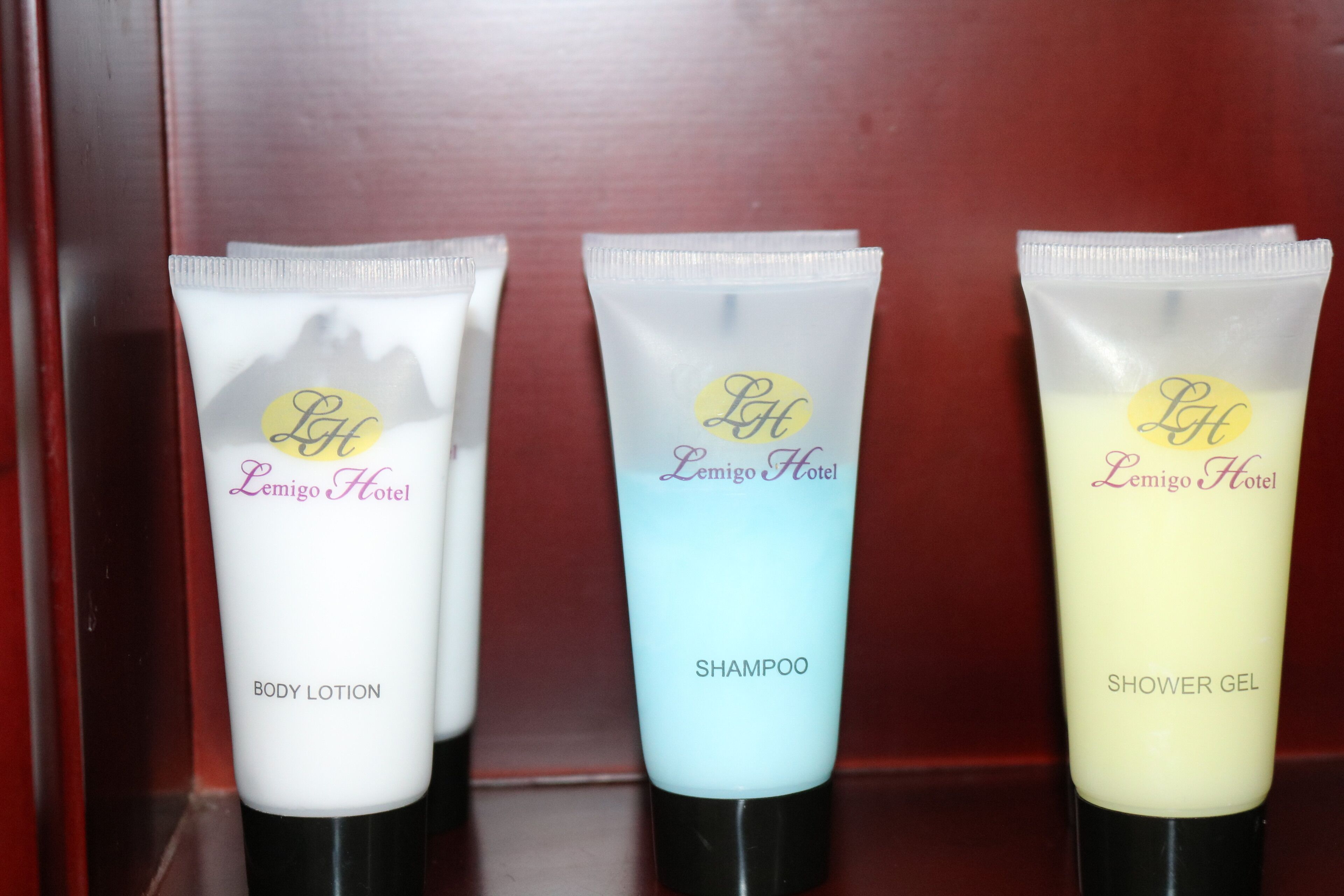 Tre toiletartiklerør mærket 'Lemigo Hotel', med teksten 'BODY LOTION', 'SHAMPOO' og 'SHOWER GEL'.