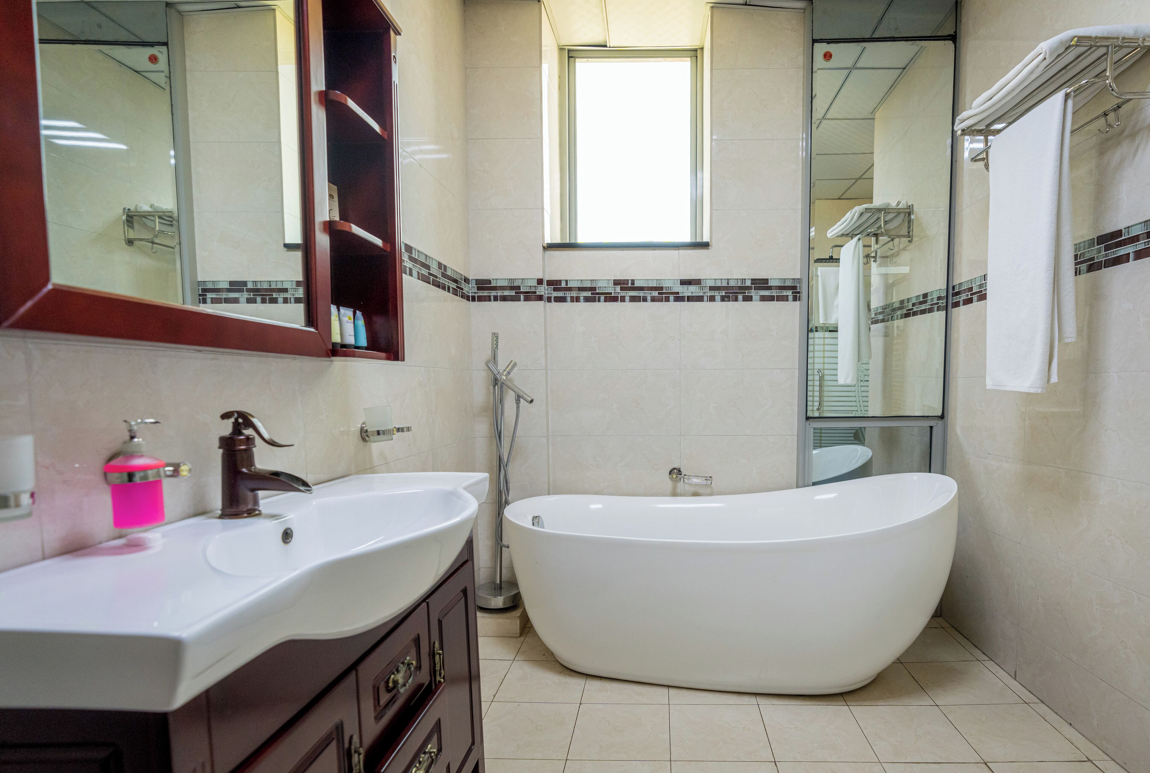 A modern bathroom with a large bathtub, two sinks, a vanity with drawers, a mirror, and a window providing natural light.
