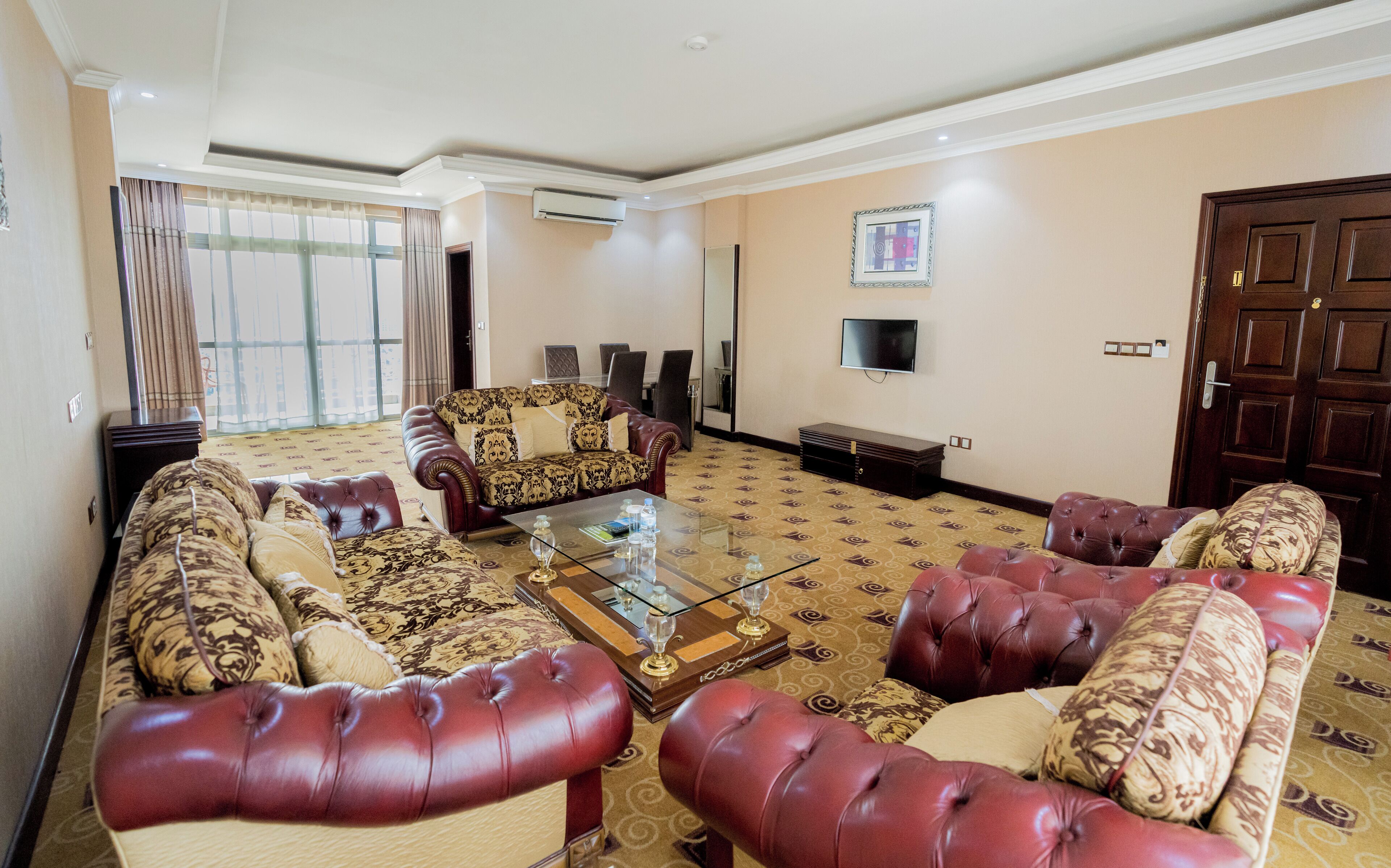 A spacious living room with a large sofa set, a glass coffee table, and a television mounted on the wall.