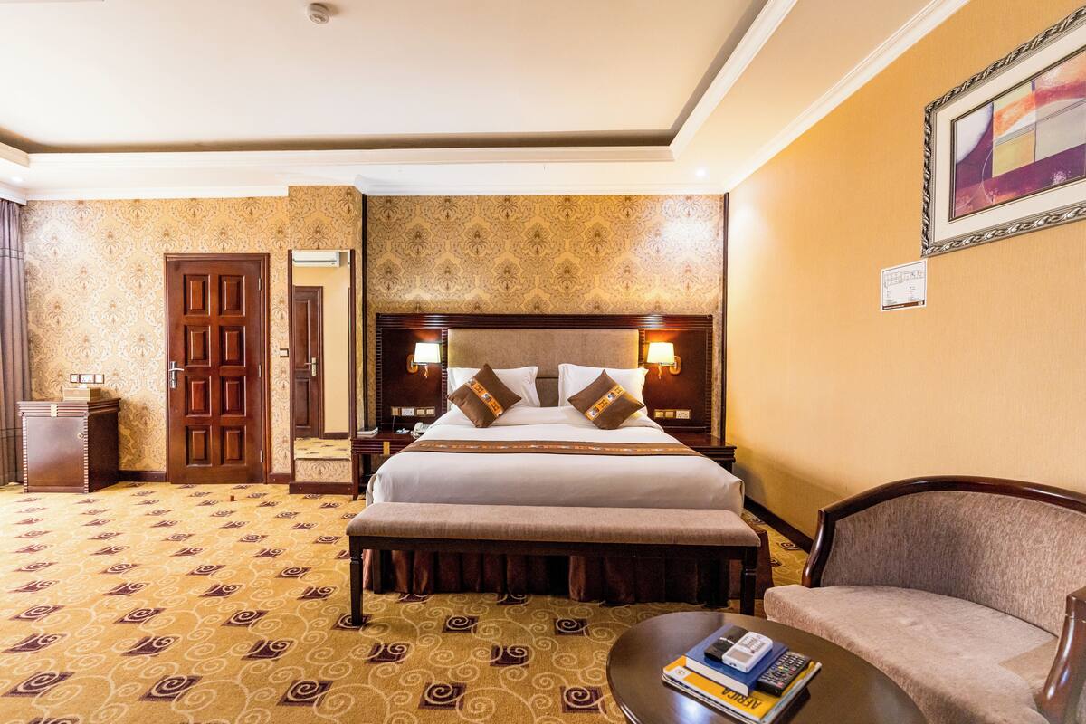 A hotel room with a large bed, a bench, a sofa, and a small table with books.