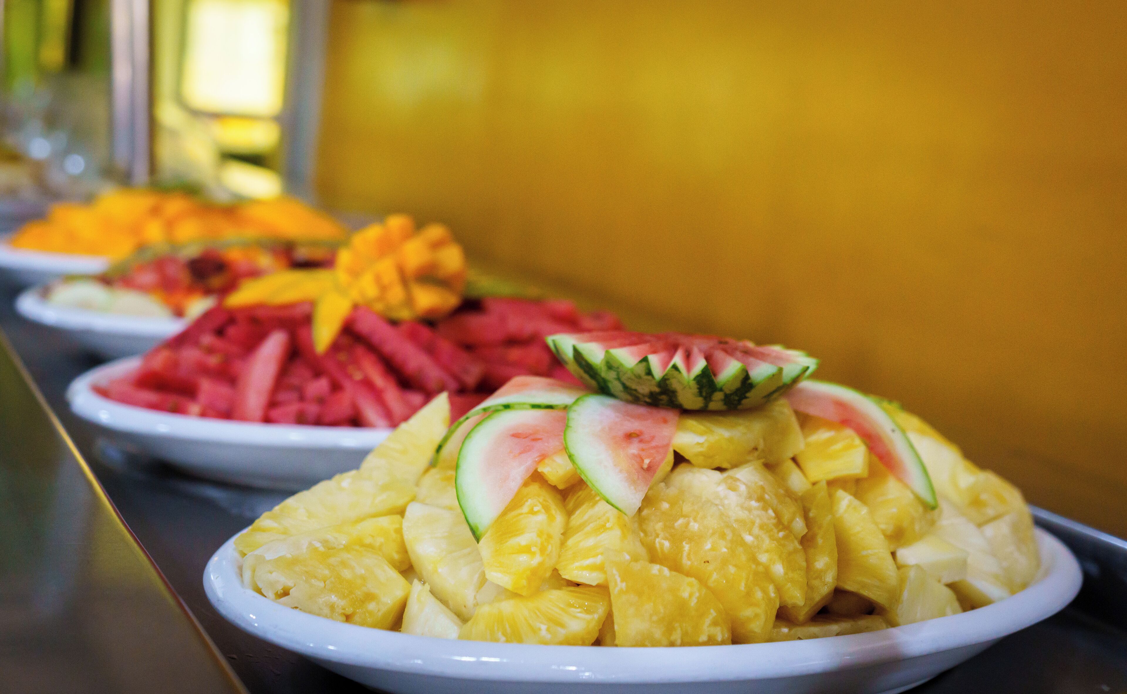 A buffet with various fruit dishes, including pineapple and watermelon.