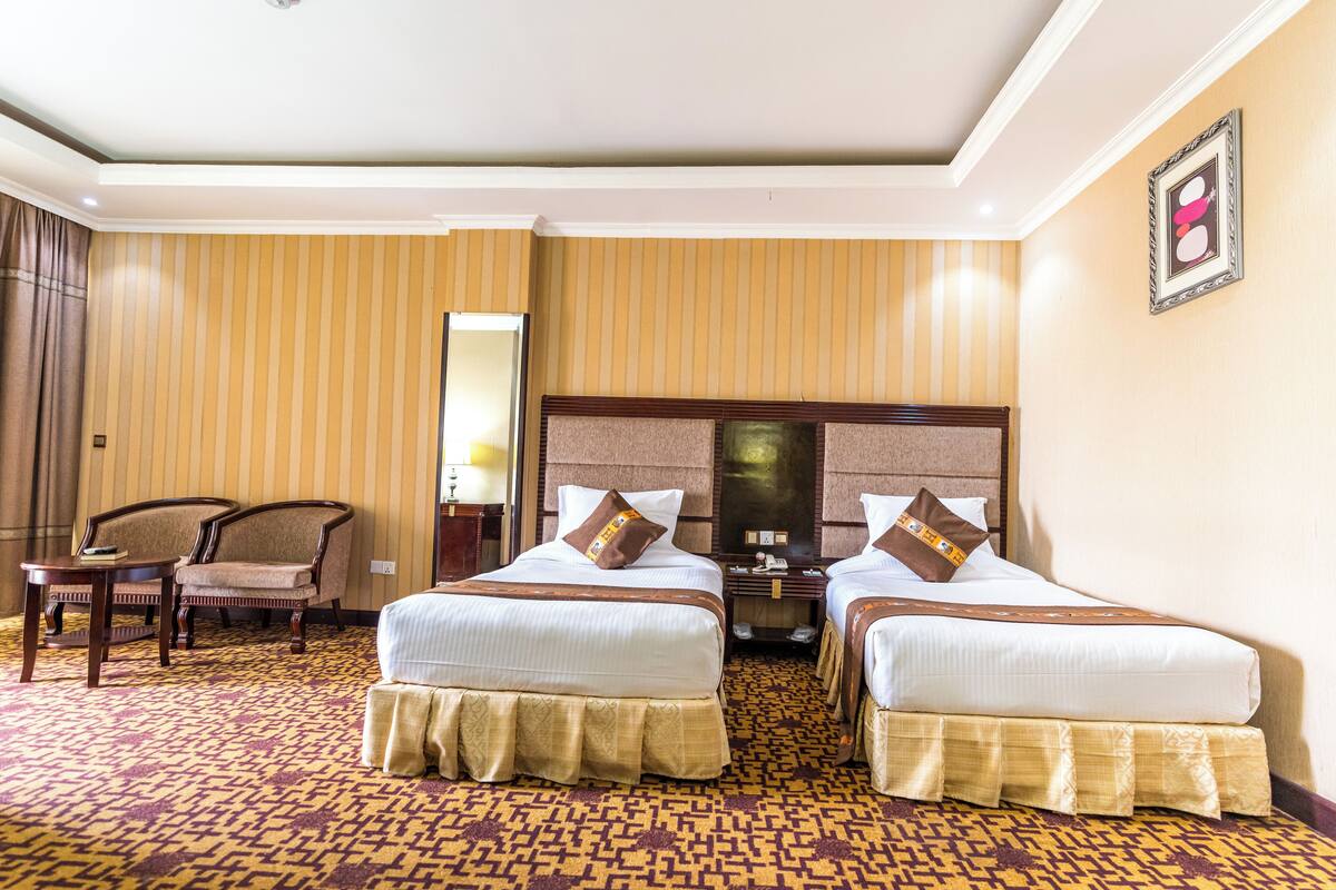 A hotel room with two beds, a sitting area with a chair, a desk, and a mirror.