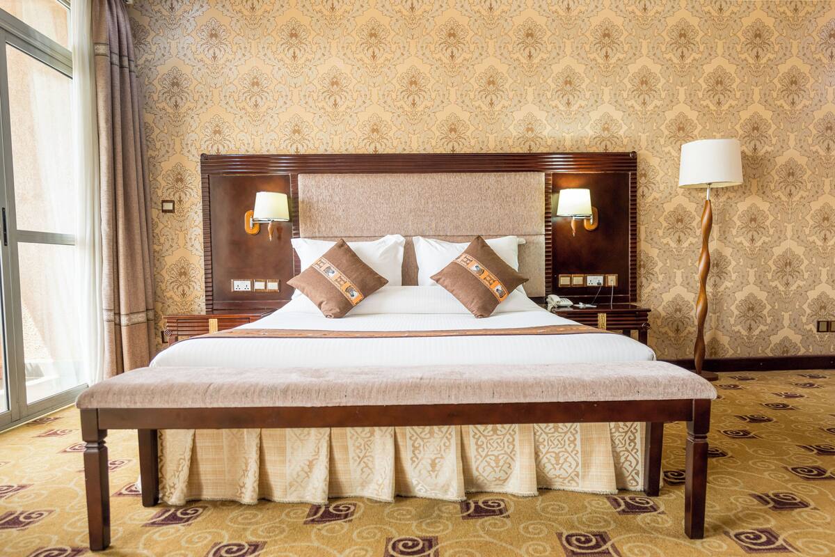 A large bed with a wooden headboard, two bedside lamps, and patterned wallpaper.