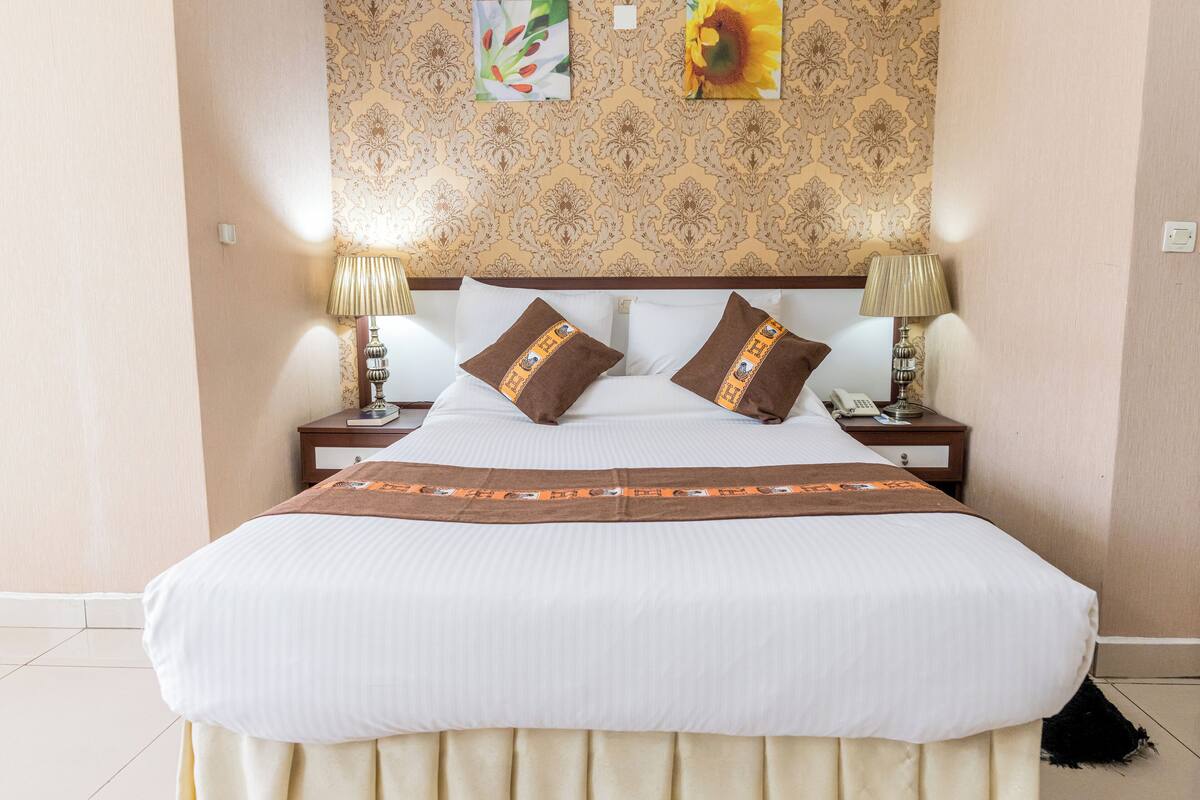 A neatly made bed with a patterned headboard, two bedside lamps, and a decorative pillow.
