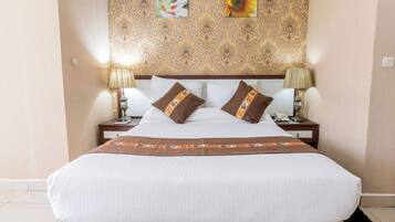Een net opgemaakt bed met een hoofdbord met patroon, twee bedlampjes en een decoratief kussen.