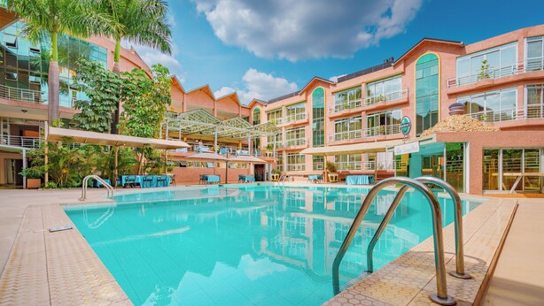 A swimming pool with a tiled deck, surrounded by a multi-story building with balconies and outdoor seating areas.