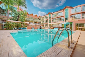 A swimming pool with a tiled deck, surrounded by a multi-story building with balconies and outdoor seating areas. - Lemigo Hotel (Kigali)