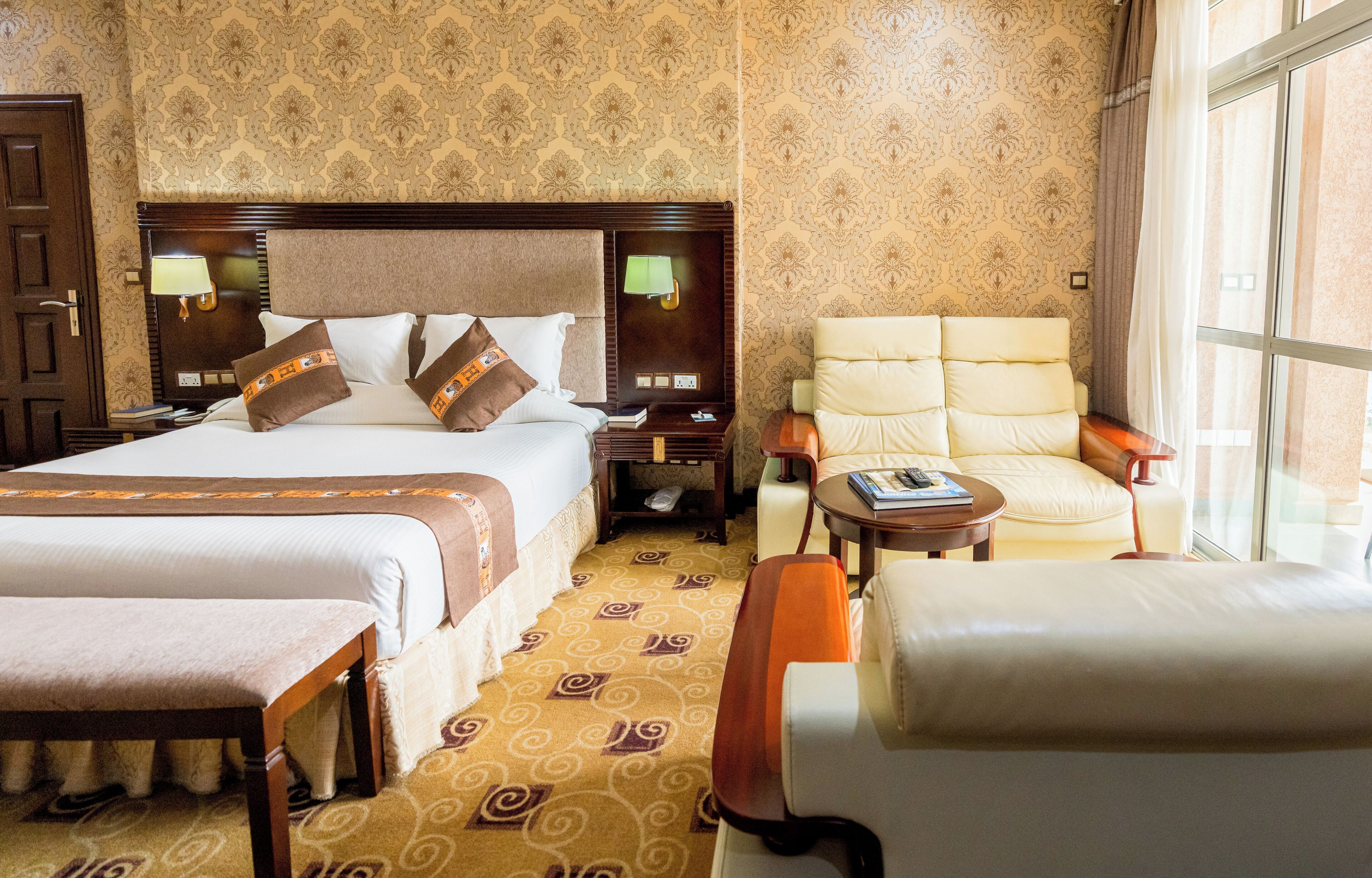 Habitación de hotel con una cama grande, dos mesitas de noche, una silla, una pequeña mesa y una ventana.