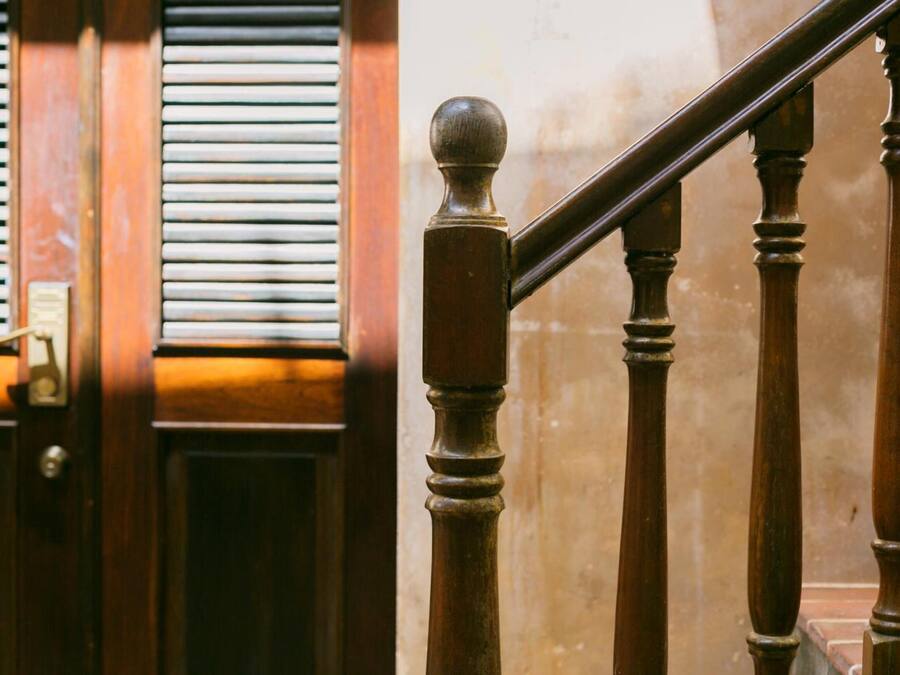 Eine Holztreppe mit Geländer und einer Tür mit Fenster und Rollläden.