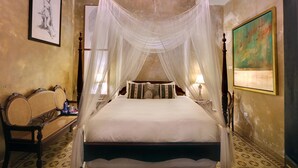Een slaapkamer met een hemelbed, een bankje, een schilderij en een kroonluchter.