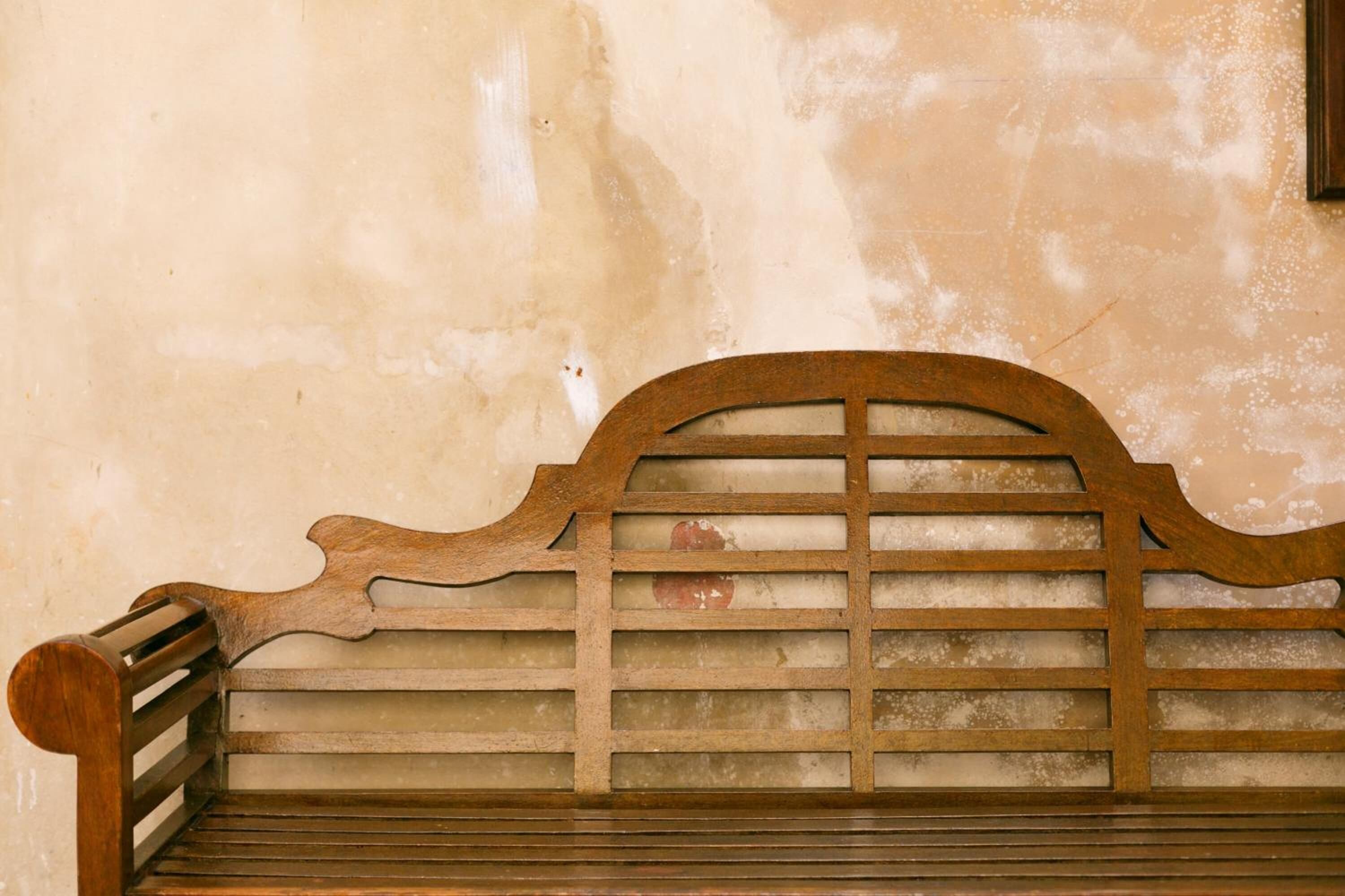 Een houten bank met een lattenleunrust tegen een structuurmuur.