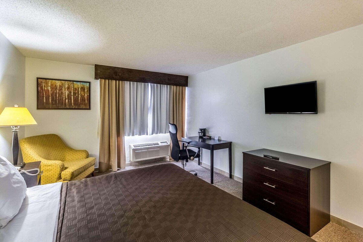 Habitación de hotel con cama, escritorio, silla, televisor y ventana con cortinas.