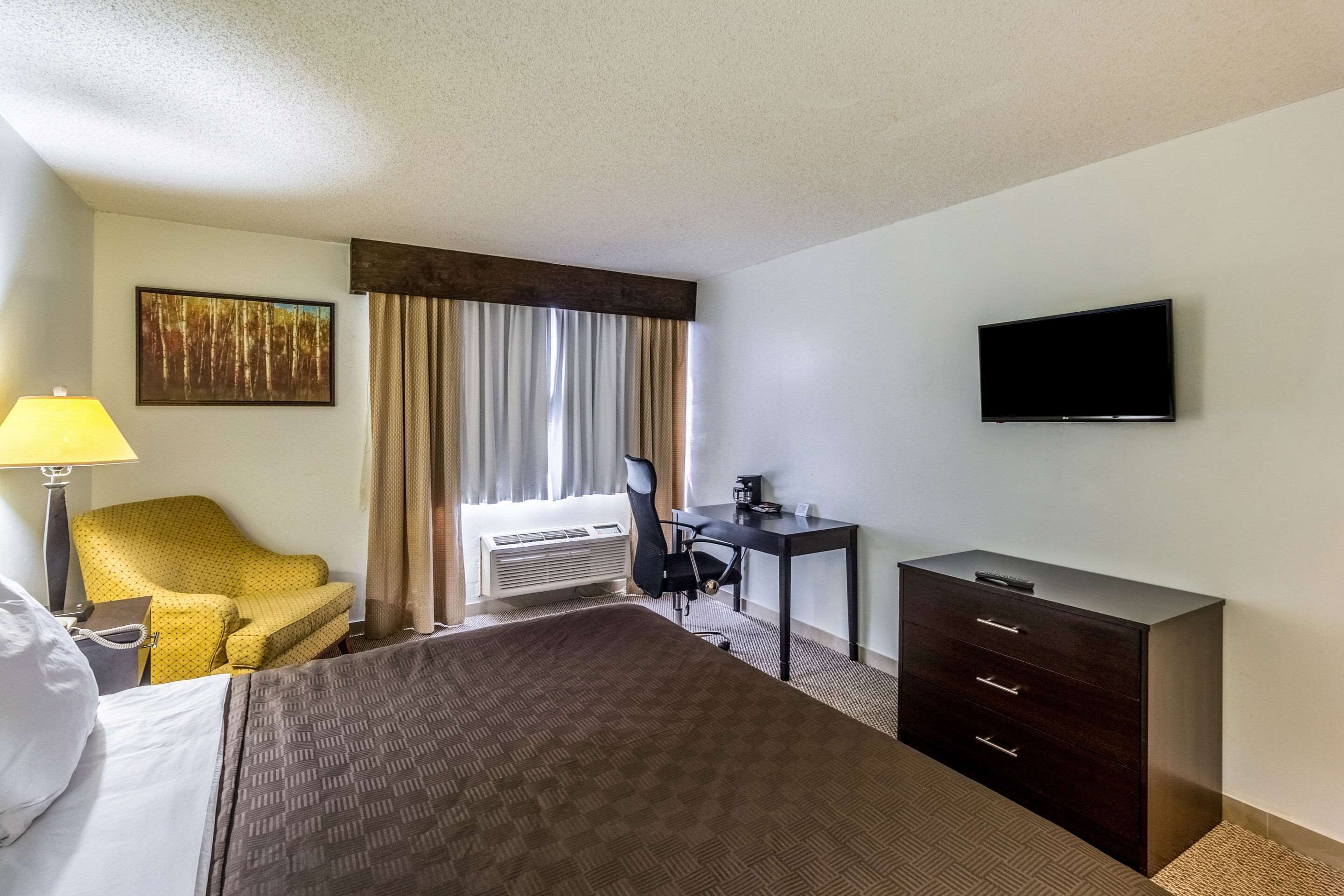 Habitación de hotel con cama, escritorio, silla, televisor y ventana con cortinas.
