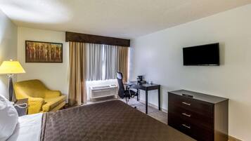 Habitación de hotel con cama, escritorio, silla, televisor y ventana con cortinas.