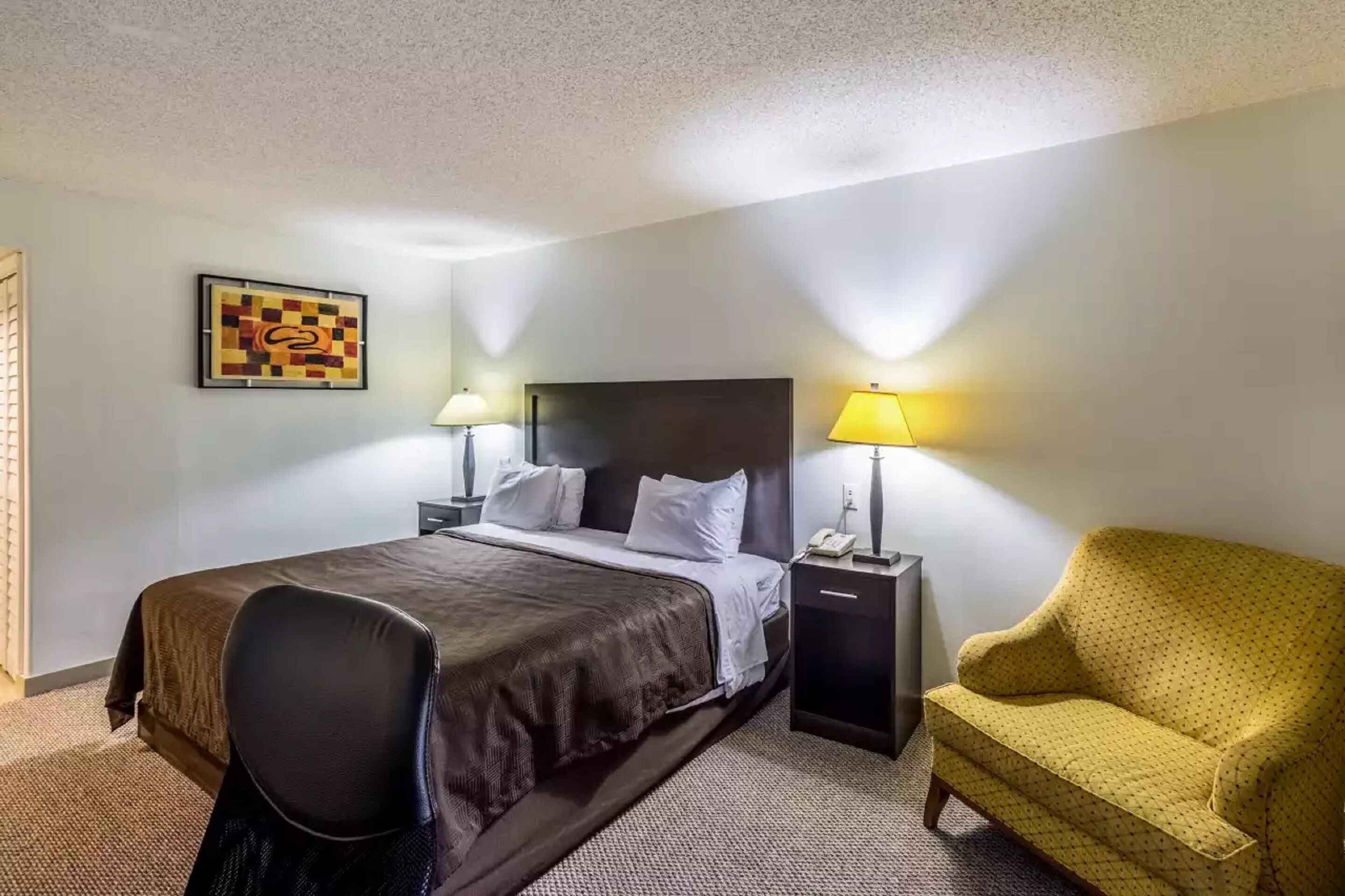Ein Hotelzimmer mit einem Bett, Nachttischlampen, einem Sessel und einem kleinen Tisch.