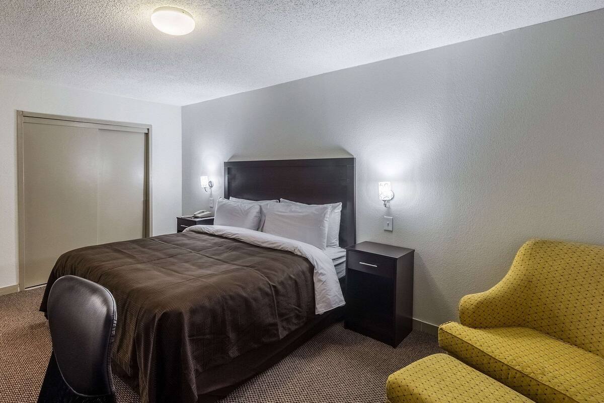 Una habitación de hotel con cama, una silla, una mesita de noche y una lámpara de pared.