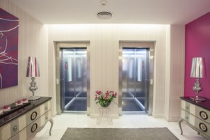 A modern elevator area with two elevators, a decorative plant, and a marble-topped console table.