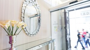 Een receptiegedeelte met een spiegel, een vaas met bloemen en een glazen deur die uitkomt op de straat.