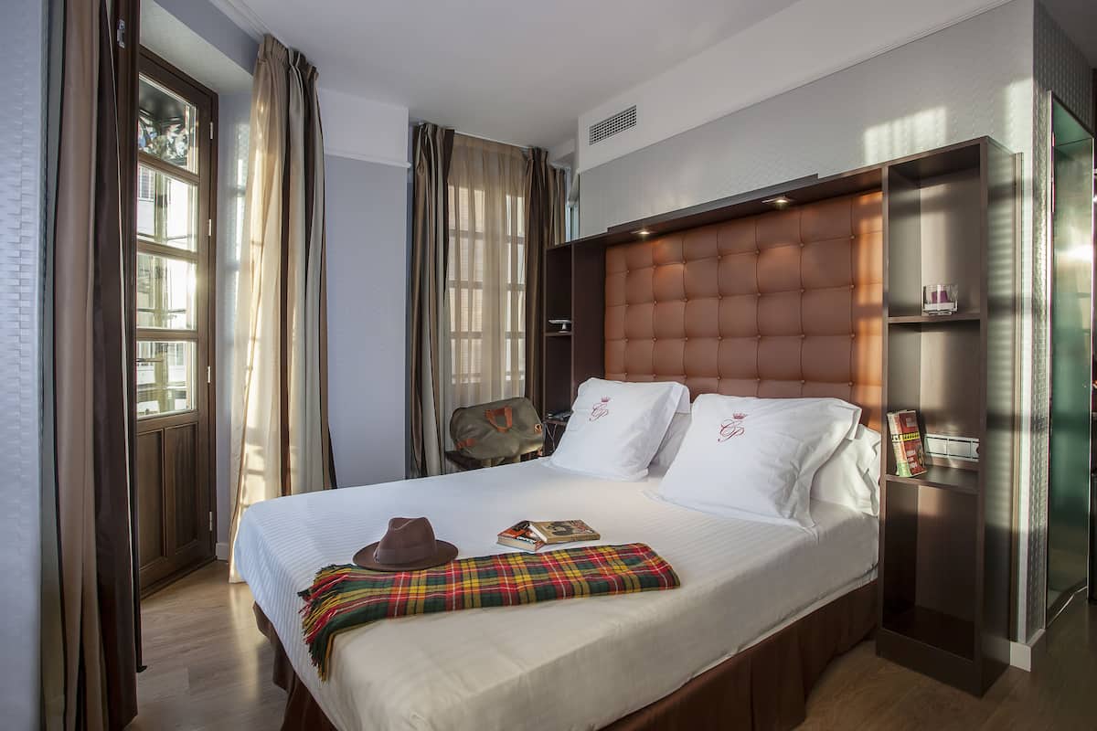 Habitación de hotel con una cama grande, cabecero, mesita de noche y una ventana con cortinas.