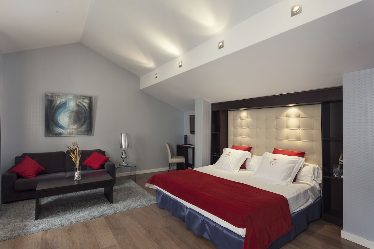 Een moderne slaapkamer met een bed, een bank, een bureau en een schilderij aan de muur.