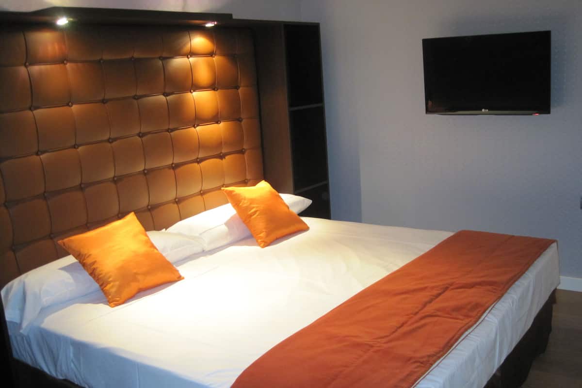 Habitación de hotel con una cama grande, cabecera con paneles iluminados y un televisor de pantalla plana montado en la pared.