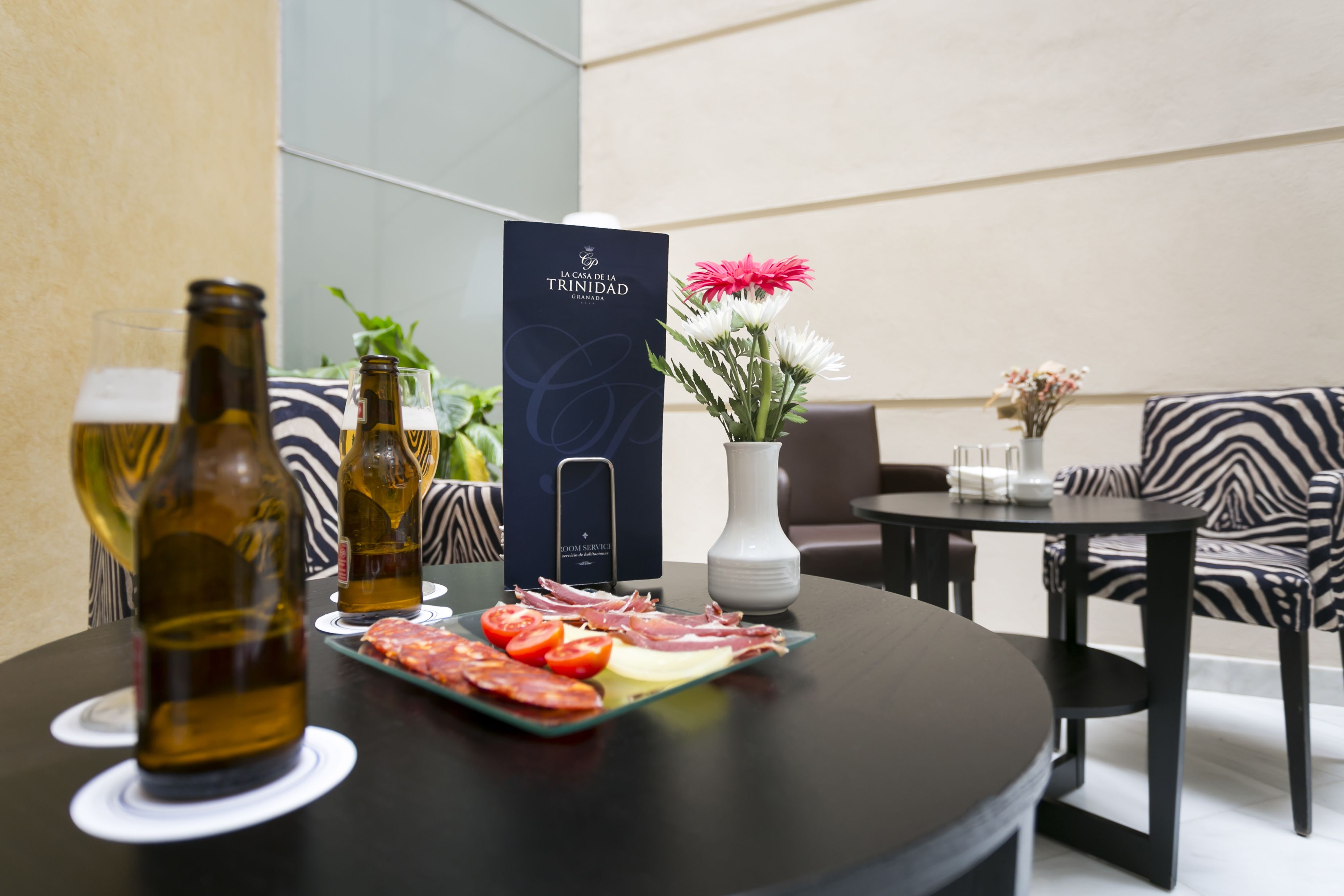 Una mesa de comedor con una cerveza, una botella de vino y un plato de comida. Hay un florero con flores y un letrero que dice 'Casa de la Trinidad Granada'.
