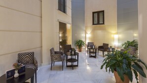Een ruime binnenruimte met verschillende zithoeken, waaronder stoelen en tafels, en potplanten.
