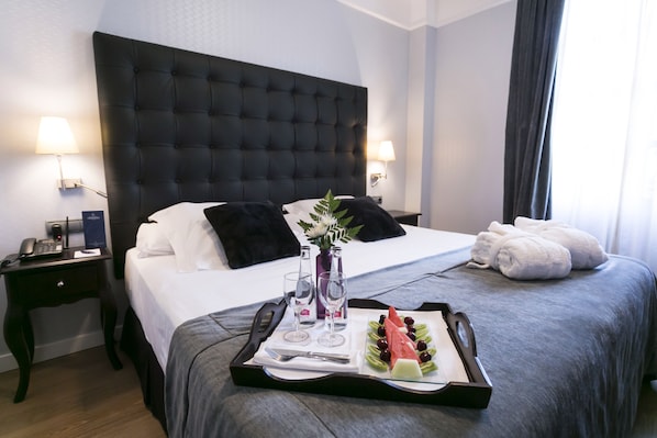 Quarto de hotel com uma cama grande, um serviço de chá com frutas e copos, e uma mesa de cabeceira com telefone e abajur.