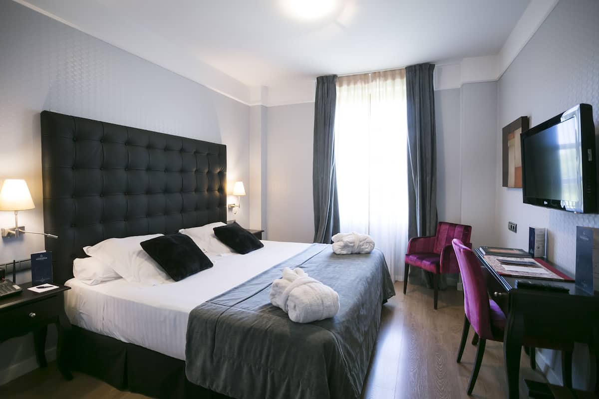 Una habitación de hotel con una cama grande, un escritorio con silla, un televisor y una ventana con cortinas.