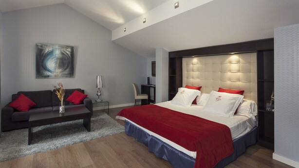 Een moderne slaapkamer met een groot bed, een donkere bank, een klein tafeltje en een schilderij aan de muur.
