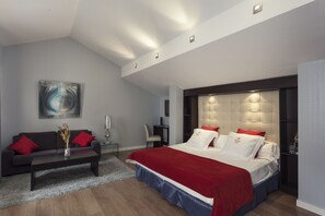Um quarto moderno com uma cama grande, um sofá escuro, uma mesinha e um quadro na parede.