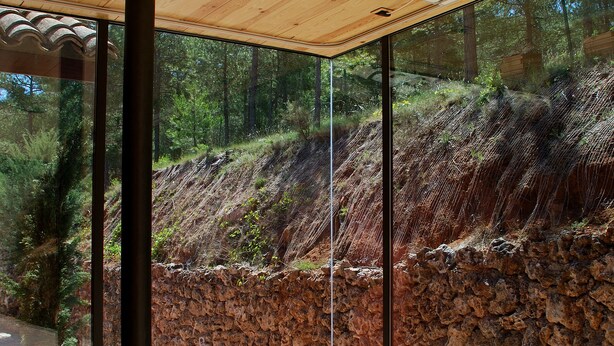 Ein modernes Interieur mit Holzboden, großen Glasfenstern und einer Steinsäule außen.
