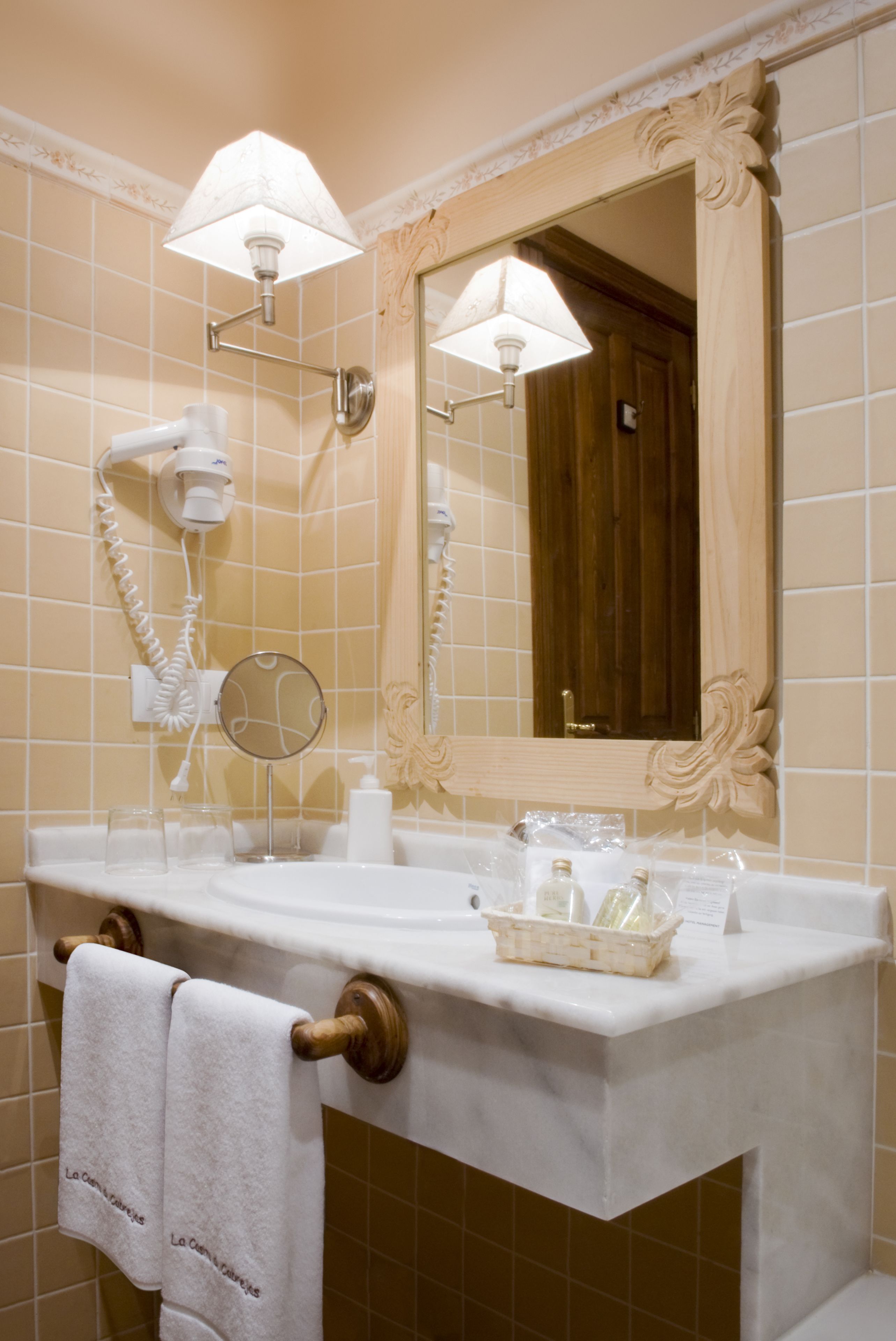 A bathroom with a white sink, two wall-mounted lamps, a mirror, and a towel rack.