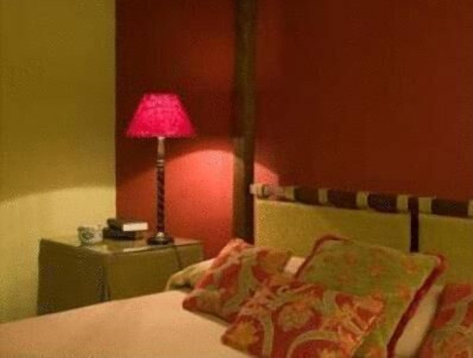 A hotel room with a bed, a nightstand, a lamp, and a red wall.