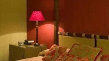 A hotel room with a bed, a nightstand, a lamp, and a red wall.