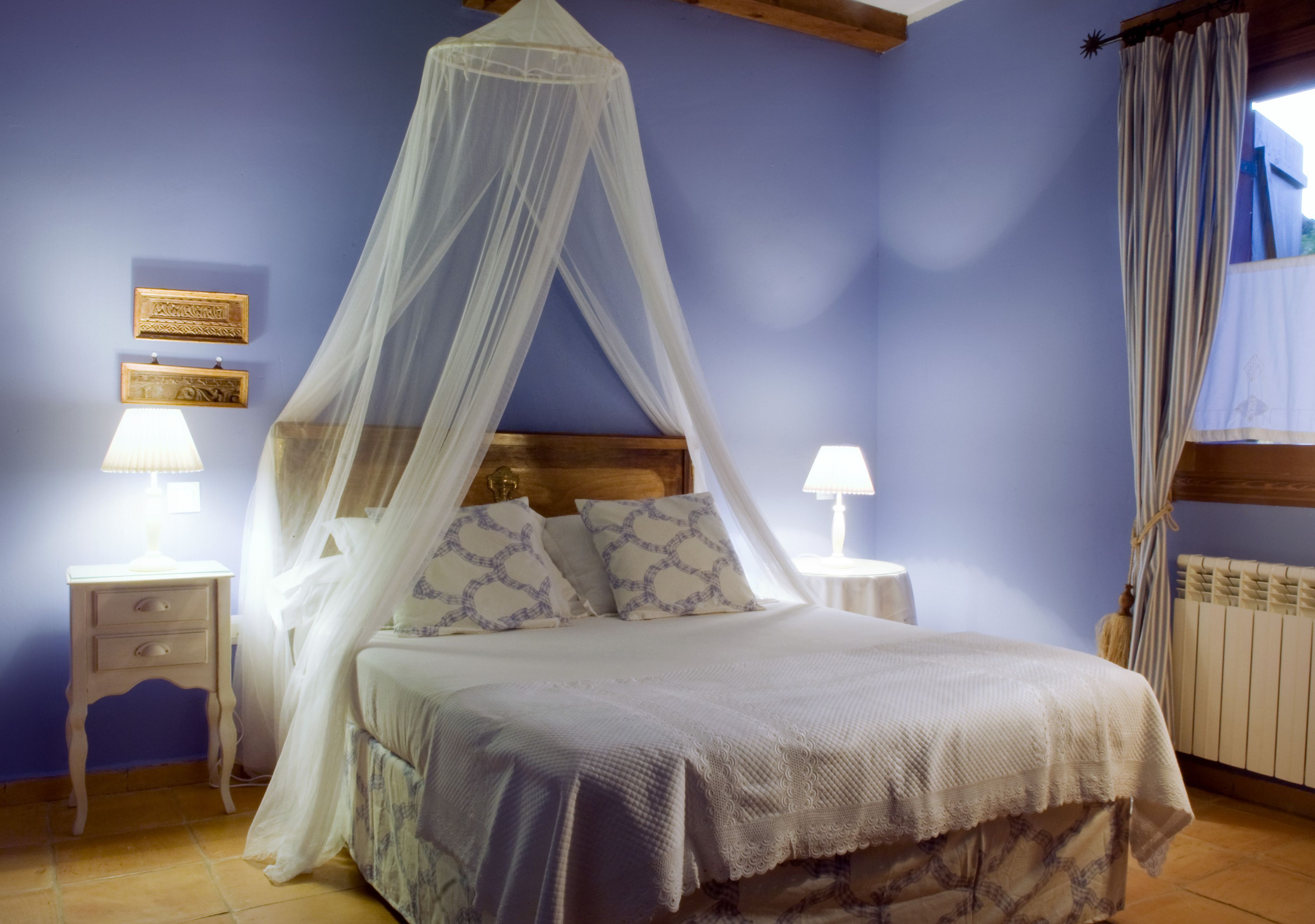 A bedroom with a canopy bed, two bedside tables with lamps, and a window with curtains.