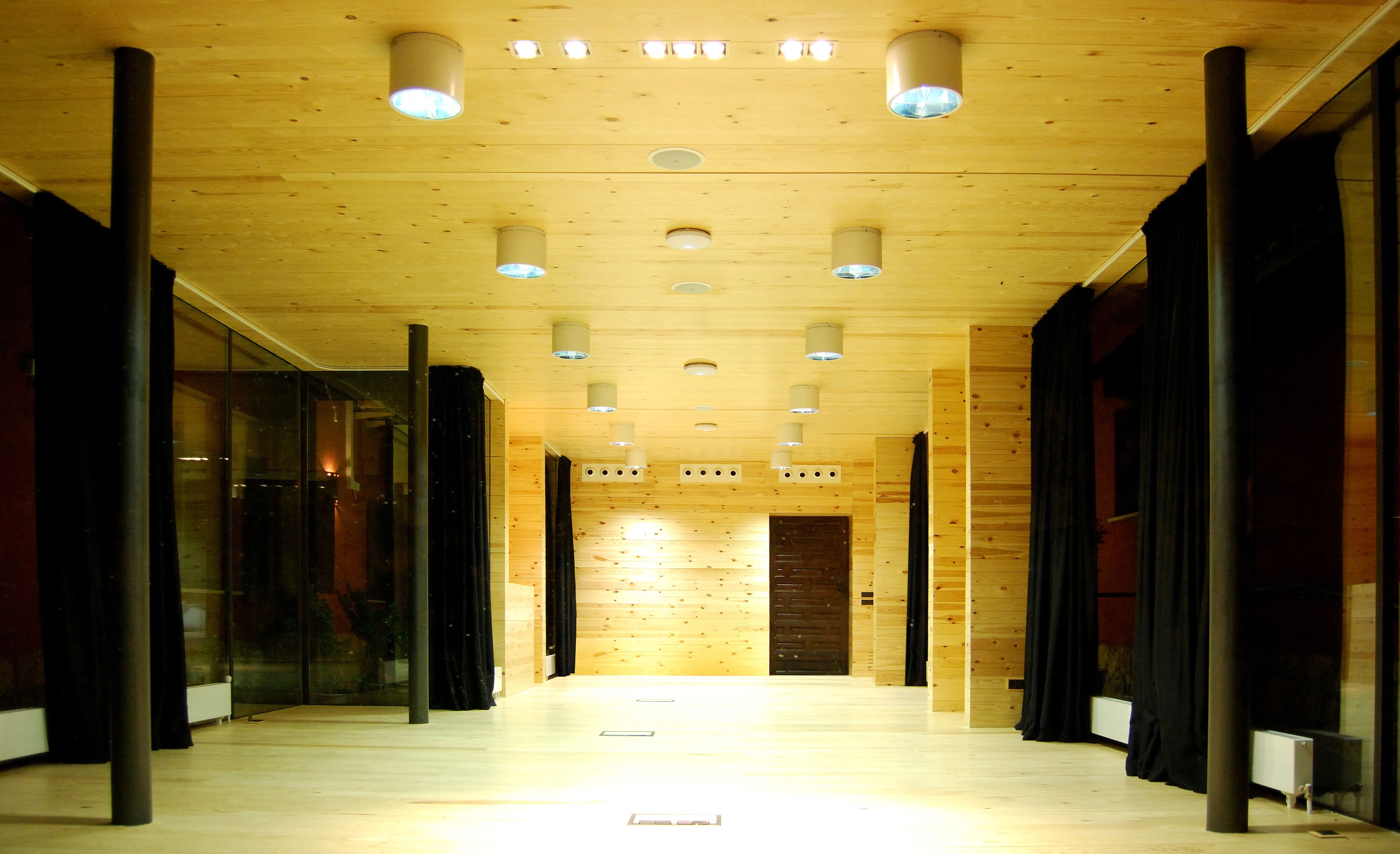A hallway with wooden paneling, recessed lighting, and glass doors on the left.