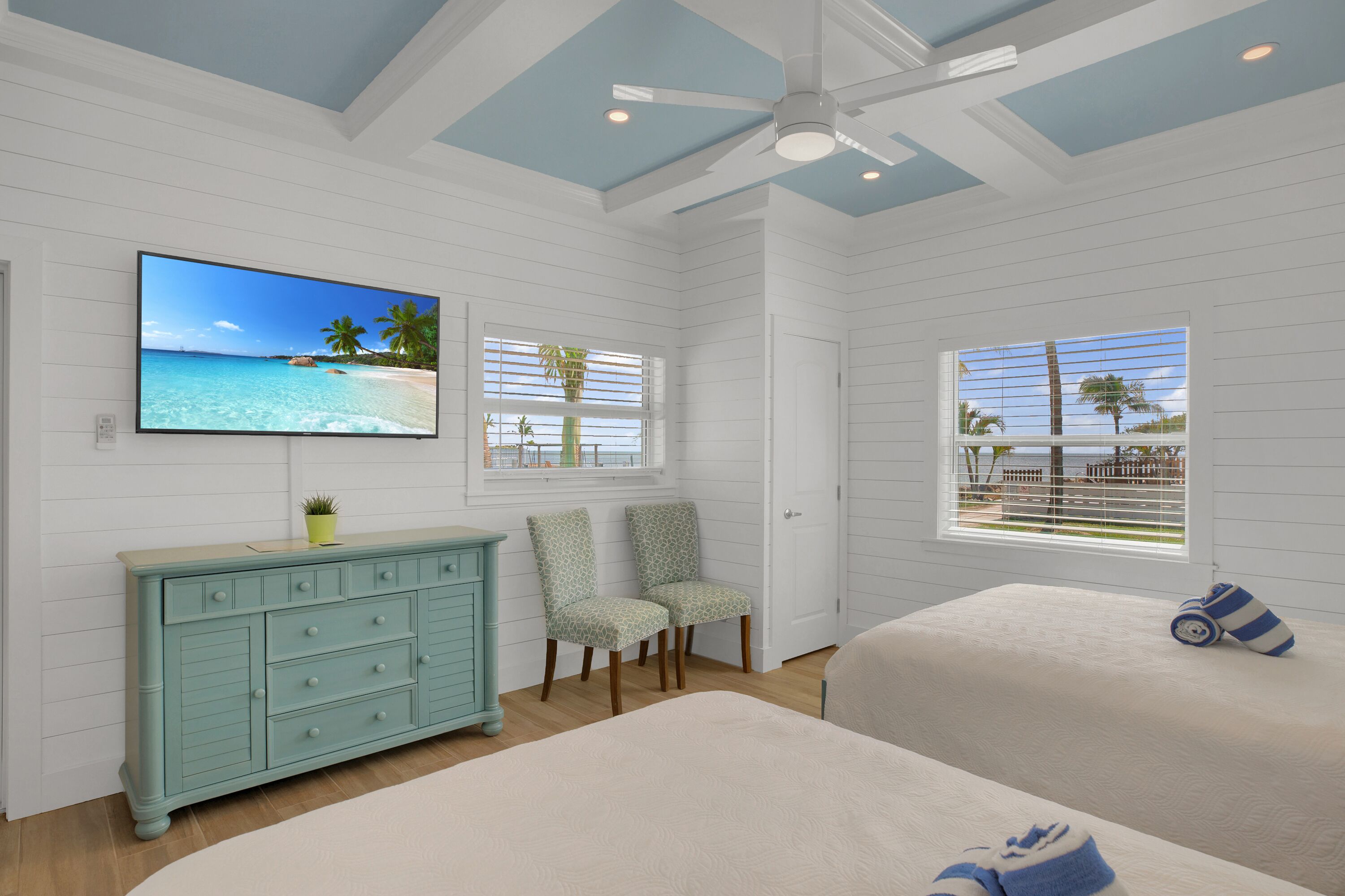 A bedroom with a TV, a dresser, two chairs, and a bed.
