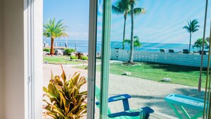 A view from a balcony overlooking a beach with palm trees, a wooden deck, and a blue picnic table. - Seascape Resort & Marina (Marathon)