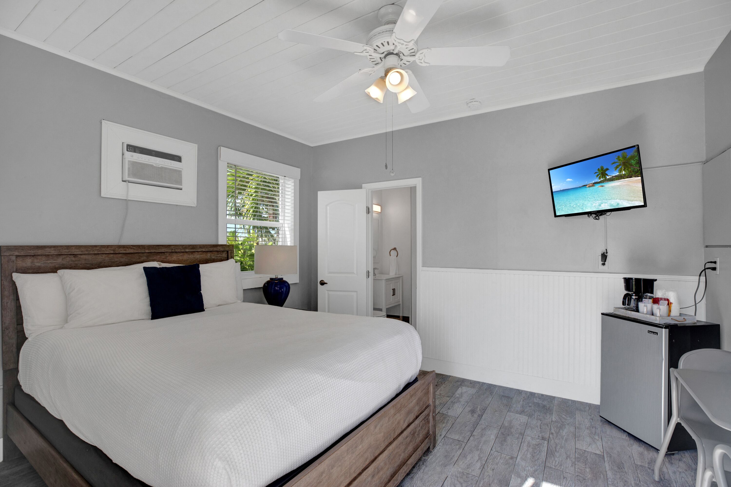 A bedroom with a bed, a desk, a TV, and a ceiling fan.